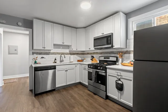 a kitchen with stainless steel appliances granite countertop a stove top oven a sink dishwasher and a refrigerator with wooden floor