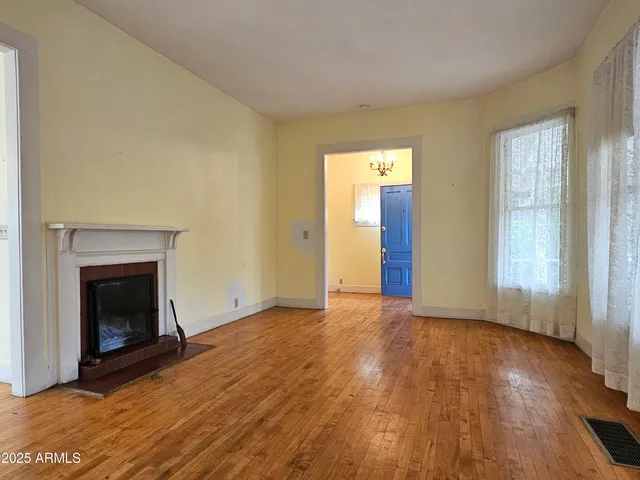 an empty room with wooden floor fireplace and windows