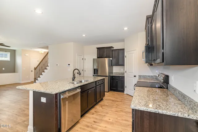 a kitchen with stainless steel appliances granite countertop a sink dishwasher a refrigerator and a oven with wooden floor