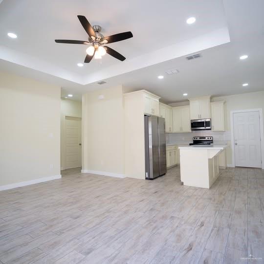 3052 Briggs Road, Unit C Weslaco, TX 78596 - Photo 2 of 16 Open concept living space featuring wood-finish flooring, a tray ceiling with recessed lighting and a ceiling fan, a full kitchen with white cabinetry and stainless steel appliances, and a kitchen island with a white countertop