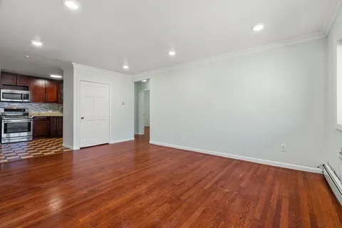 a view of an empty room with wooden floor and a kitchen