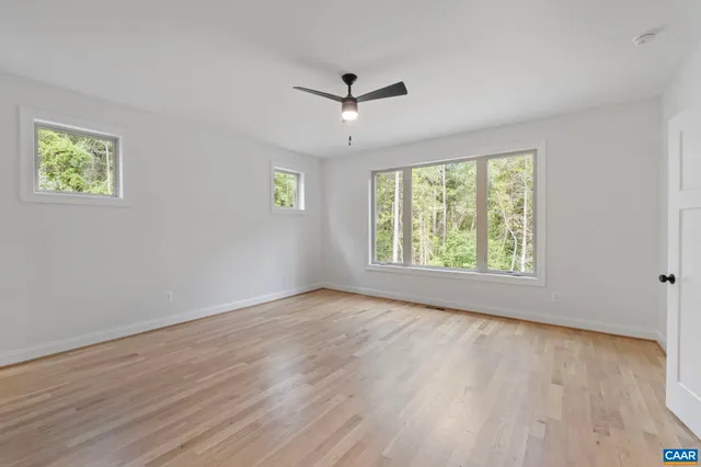 an empty room with wooden floor ceiling fan and windows