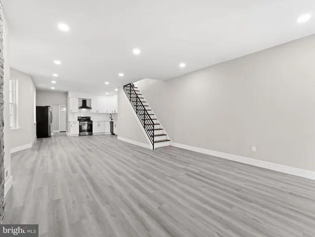 a view of an empty room with wooden floor stairs and a way to kitchen