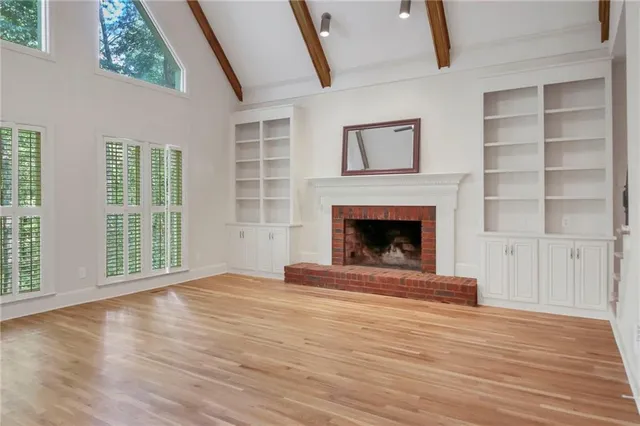 a view of an empty room with wooden floor fireplace and a window