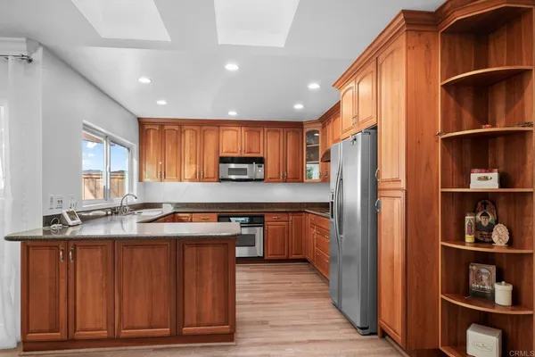 a kitchen with stainless steel appliances granite countertop a refrigerator a sink dishwasher and wooden cabinets with wooden floor