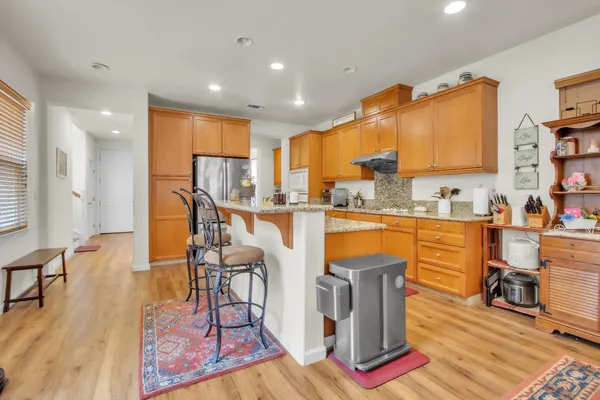 a kitchen with stainless steel appliances granite countertop a refrigerator a stove top oven and a dining table with wooden floor