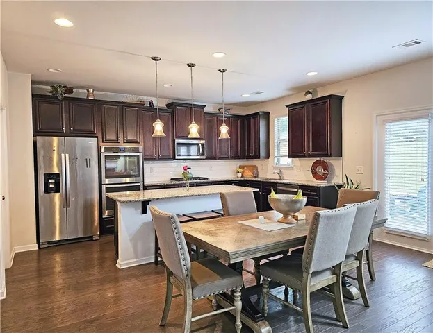 a kitchen with stainless steel appliances kitchen island granite countertop a dining table chairs refrigerator and microwave