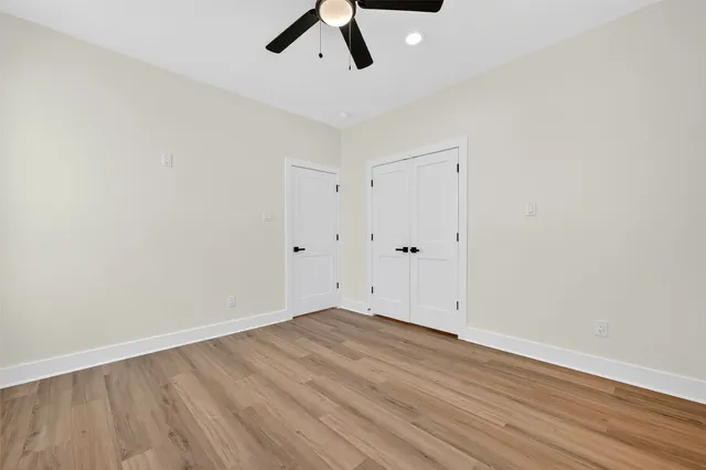 an empty room with wooden floor chandelier fan and windows