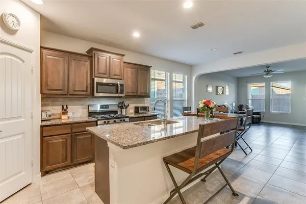 a kitchen with stainless steel appliances granite countertop a stove top oven a sink dishwasher a dining table and chairs with wooden floor