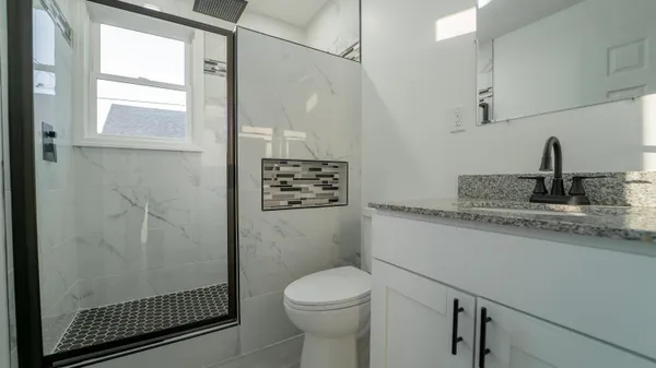 a bathroom with a granite countertop sink a toilet a mirror and shower