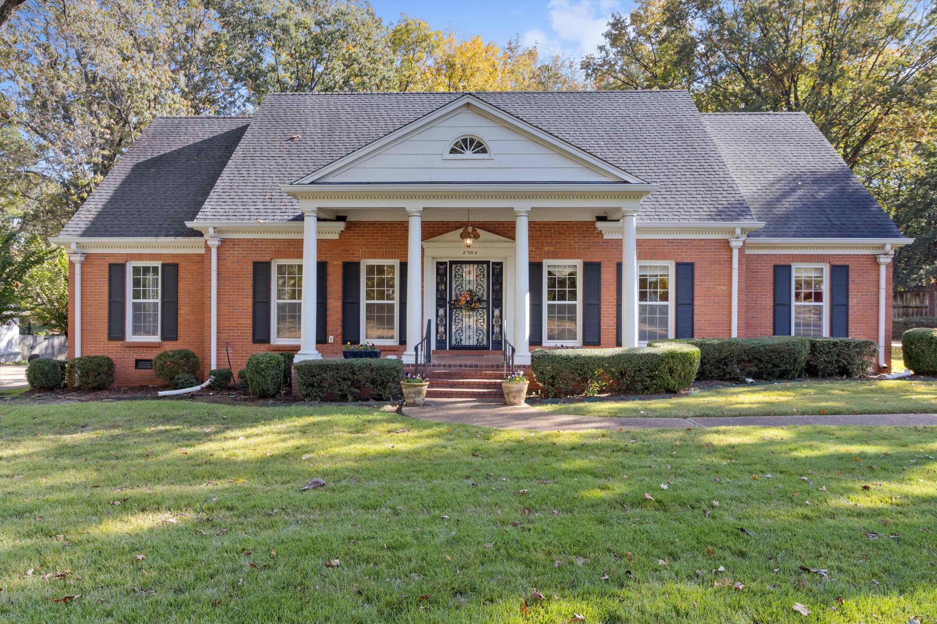Neoclassical / greek revival house featuring a front lawn, brick siding, covered porch, and roof with shingles