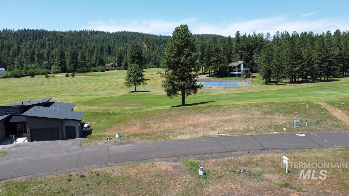 View of property's community with view of golf course, a forest view, a lawn, and a garage