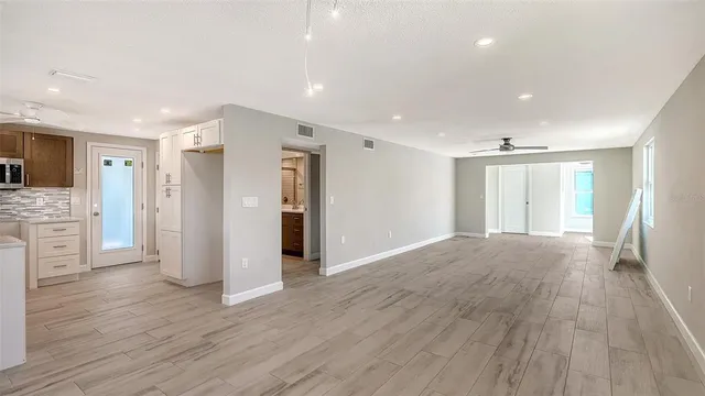 a view of an empty room with wooden floor and a kitchen