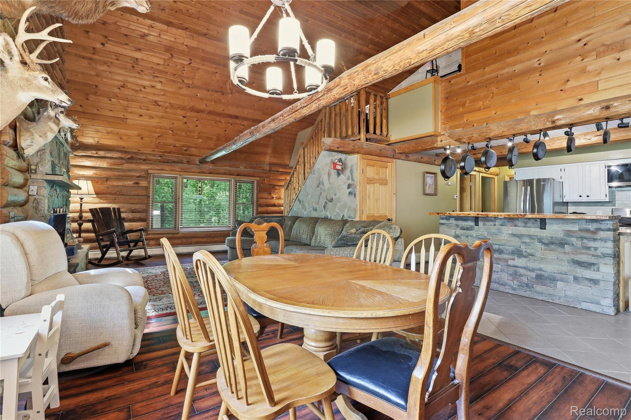 Open-concept living space featuring wood-finish flooring, a stone-clad fireplace, and a kitchen island with stone detailing