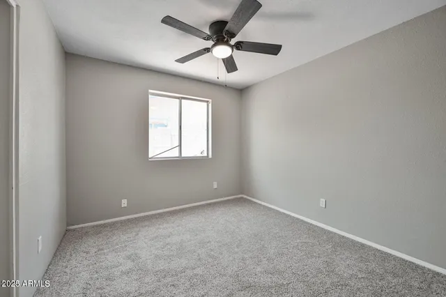 an empty room with a chandelier fan and windows
