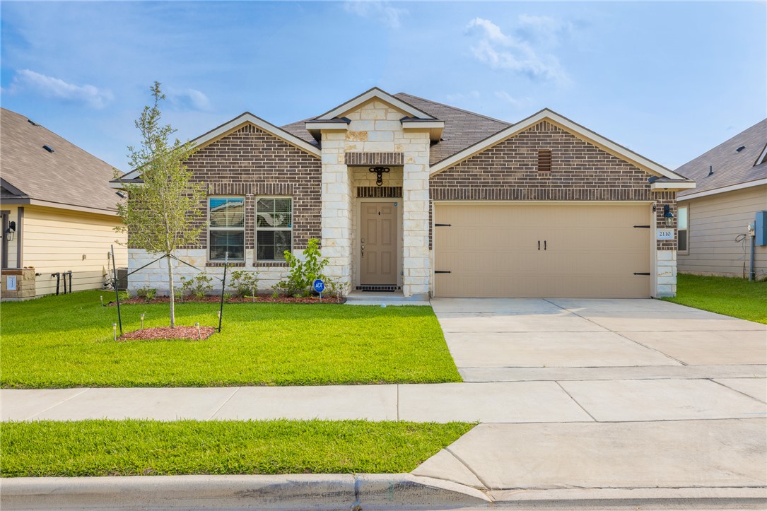 View of front of property with a front lawn, concrete driveway, brick siding, stone siding, and an attached garage