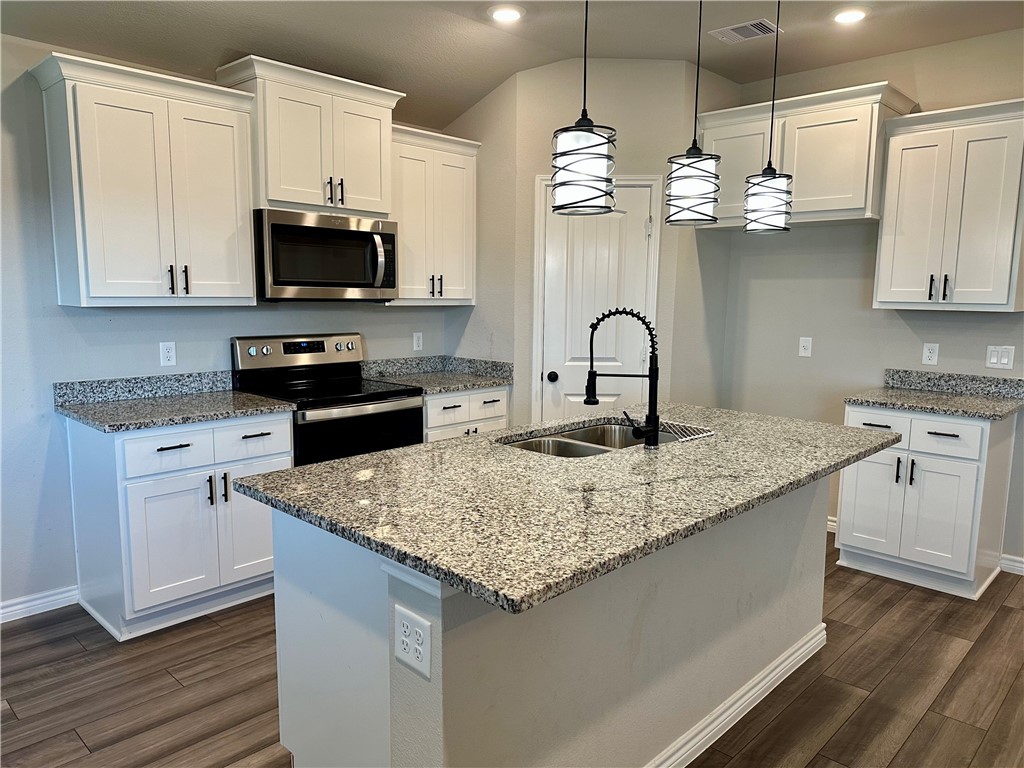 2110 Chief Street Bryan, TX 77807 - Photo 4 of 16 Kitchen with stainless steel appliances, light stone counters, white cabinetry, hanging light fixtures, and a kitchen island with sink