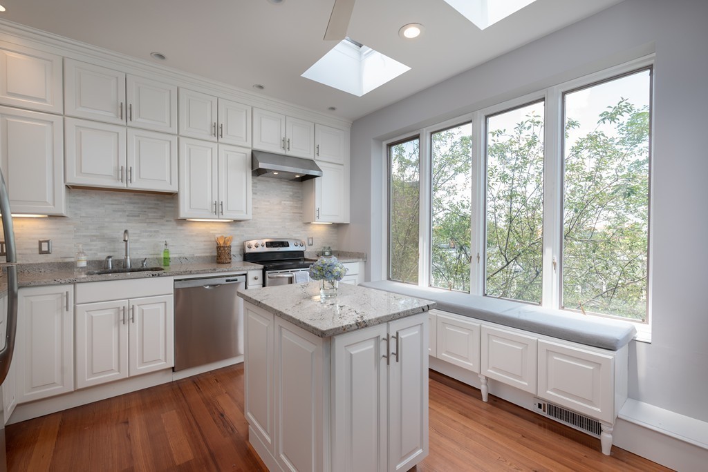 a kitchen with a stove a sink and white cabinets with wooden floor next to windows