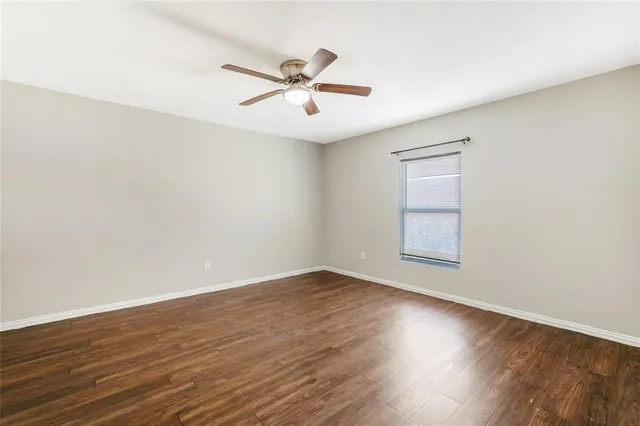 an empty room with wooden floor fan and windows
