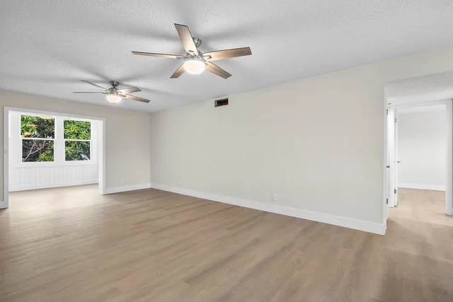 an empty room with wooden floor chandelier fan and windows
