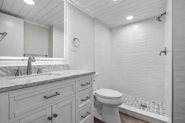 a bathroom with a granite countertop toilet a sink a mirror and shower