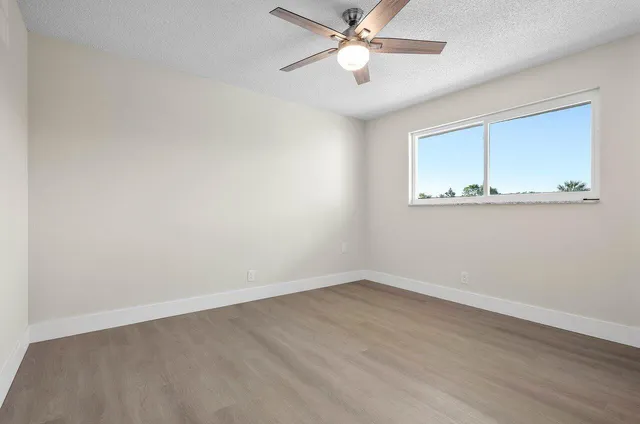 an empty room with wooden floor fan and windows