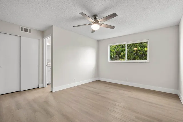 a view of an empty room with wooden floor and a ceiling fan