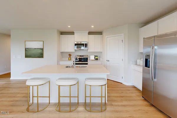 a kitchen with stainless steel appliances granite countertop a sink a microwave a refrigerator and white cabinets with wooden floor