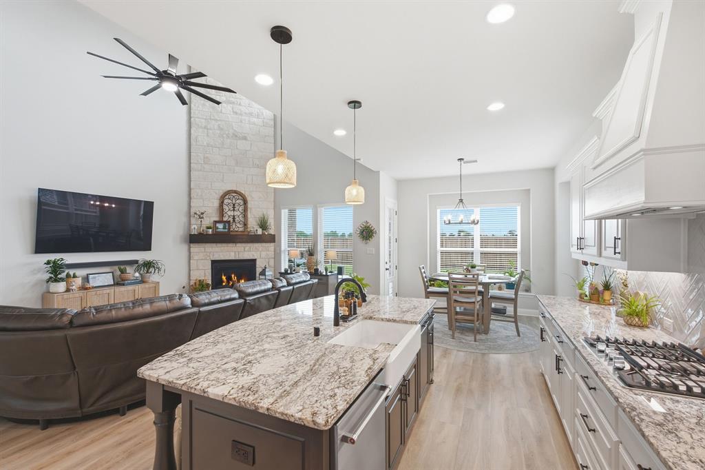 313 Tate Lane Anna, TX 75409 - Photo 10 of 30 Open-concept living space featuring a central kitchen island with granite countertops and a farmhouse sink, stainless steel appliances, and wood-finish flooring