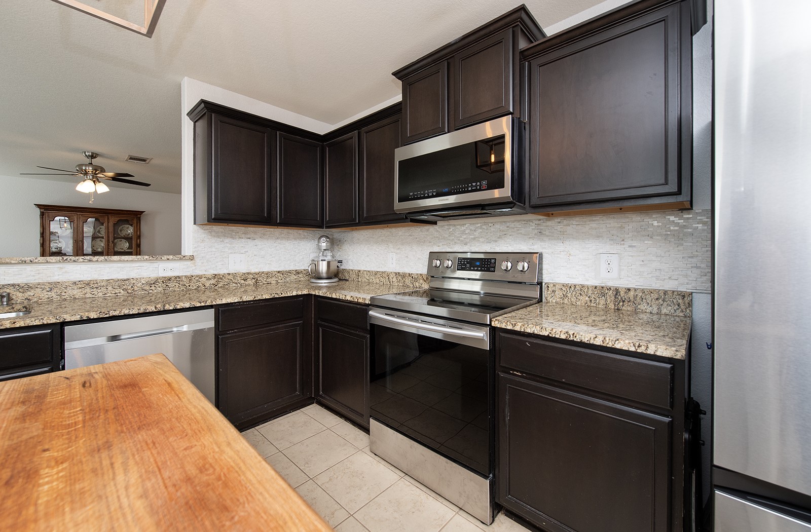 216 Millers Loop Jarrell, TX 76537 - Photo 8 of 31 Kitchen featuring stainless steel appliances, granite counter, tile flooring, backsplash, and dark brown cabinetry