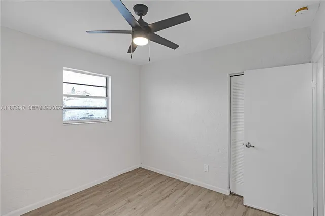 an empty room with wooden floor chandelier fan and windows