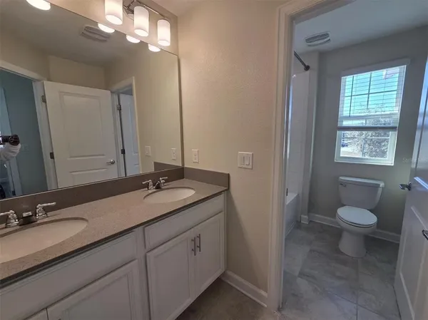 a bathroom with a granite countertop sink a toilet a mirror and window