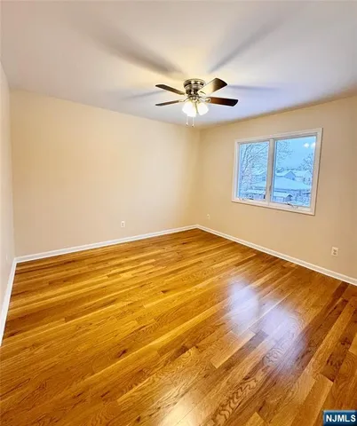 a view of an empty room with wooden floor and a ceiling fan