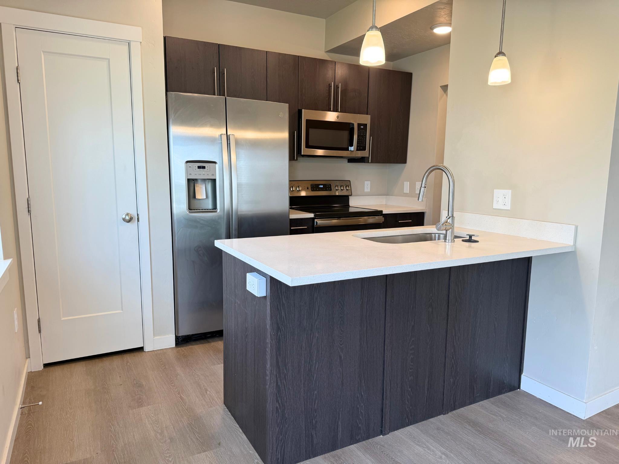 616 North 44th Street Nampa, ID 83687 - Photo 4 of 18 Kitchen with appliances with stainless steel finishes, dark brown cabinets, a peninsula, hanging light fixtures, and light wood finished floors