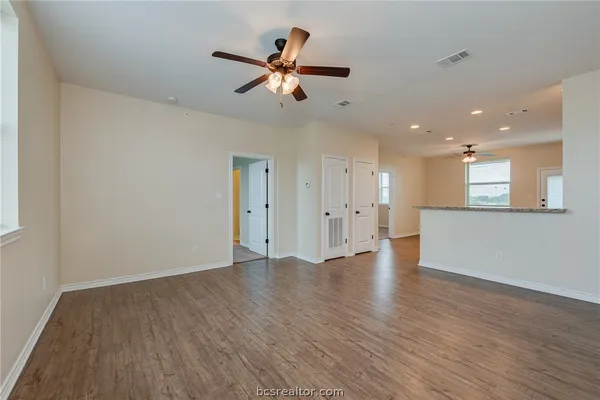 a view of an empty room with wooden floor and a ceiling fan