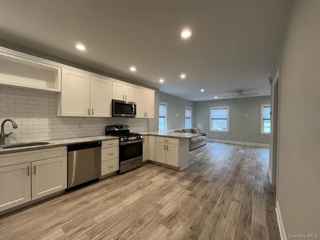 an empty room with wooden floor and way to kitchen