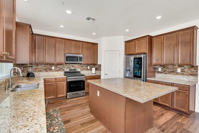 a kitchen with stainless steel appliances granite countertop a stove top oven a sink dishwasher and a refrigerator with wooden cabinets