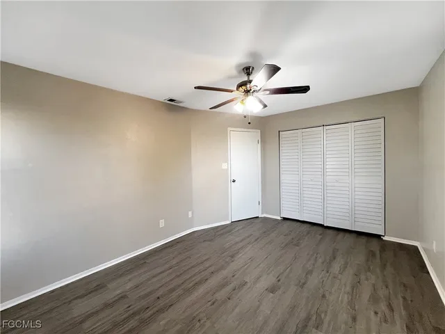 a view of an empty room with wooden floor and a ceiling fan