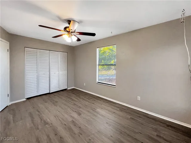 an empty room with wooden floor chandelier fan and windows