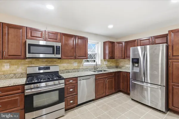 a kitchen with stainless steel appliances granite countertop a stove top oven a refrigerator and a sink with wooden floor