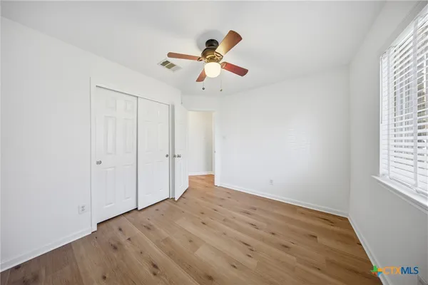 an empty room with wooden floor ceiling fan and window