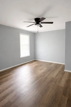 an empty room with wooden floor ceiling fan and windows