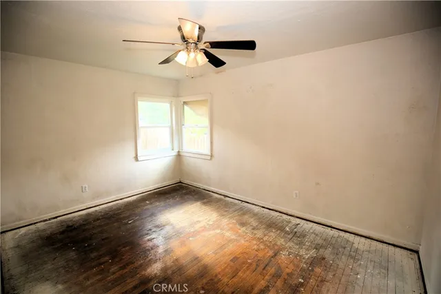 an empty room with wooden floor fan and windows