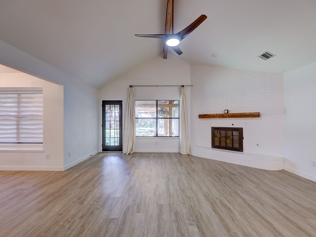 5842 Secrest Drive Austin, TX 78759 - Photo 11 of 40 Vast main living space with vaulted ceilings, a central ceiling fan, and a cozy fireplace.