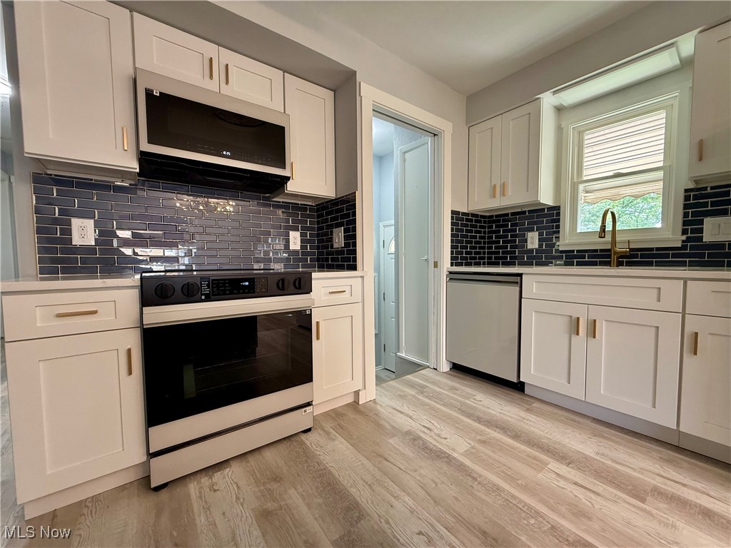 19504 Sumpter Road Cleveland, OH 44128 - Photo 11 of 39 Kitchen with white cabinets, electric range oven, white microwave, and tasteful backsplash