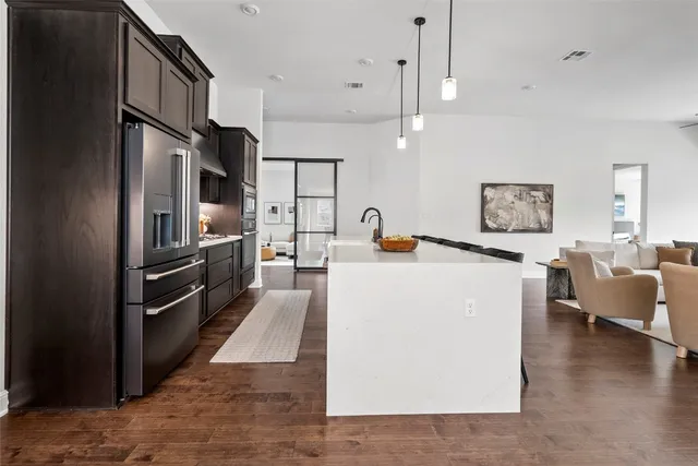 a large kitchen with stainless steel appliances kitchen island a stove a refrigerator a couch and a dining table with wooden floor