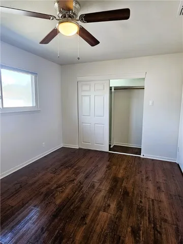 a view of an empty room with chandelier fan and wooden floor