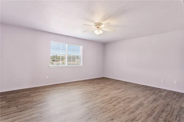 an empty room with wooden floor chandelier fan and windows