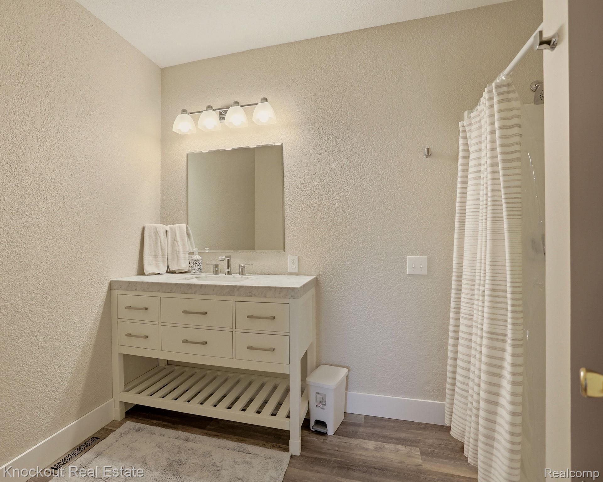9941 Lange Road Birch Run, MI 48415 - Photo 27 of 42 Bathroom featuring a single vanity with a light-toned countertop, wood-finish flooring, a wall-mounted light fixture, and a shower with a curtain rod