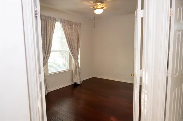 an empty room with wooden floor and windows with curtains